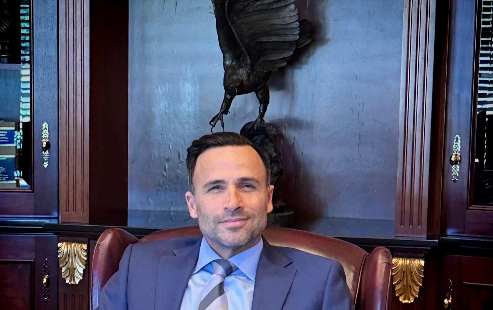 A man in suit and tie sitting in front of a statue.